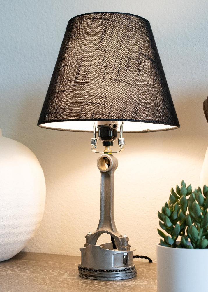 Table lamp with a black shade on a wooden surface next to a potted plant.