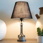 Table lamp with black shade on a wooden surface next to a plant and decorative items.