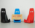 Three car seat models in black, blue, and red with a cardboard sign in the center on a white surface.