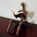 Pipe sculpture with a light bulb head reading a book on a wooden surface.