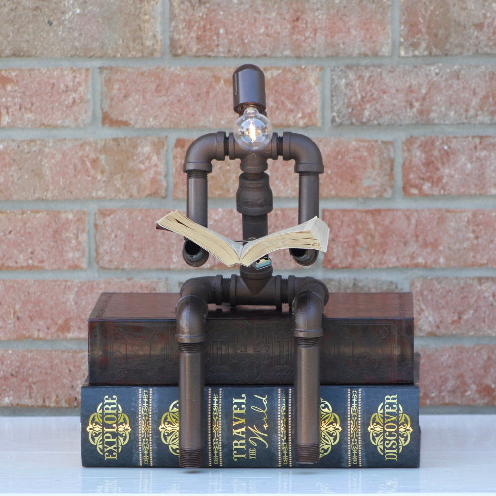 Decorative lamp made of pipes and books against a brick wall.