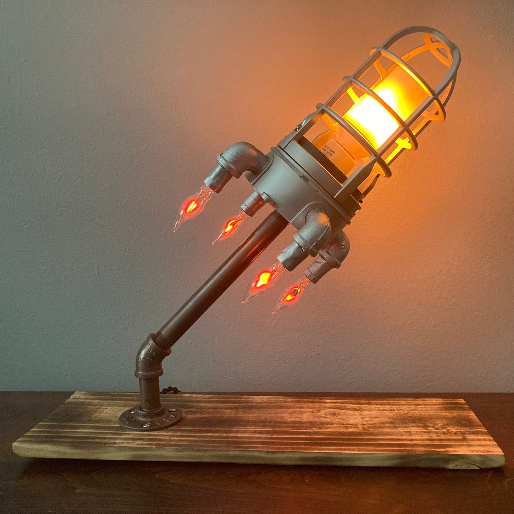Industrial-style lamp with glowing bulb on a wooden base against a plain background
