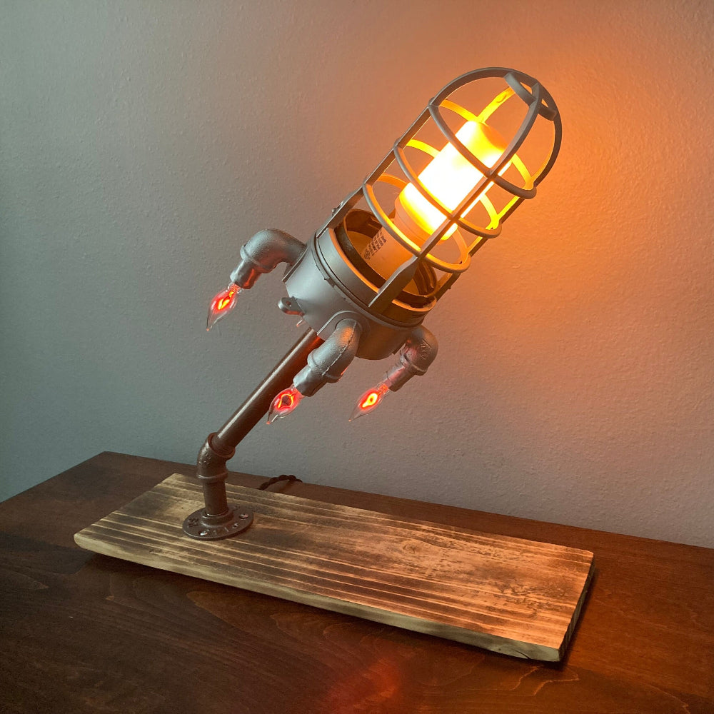 Industrial-style lamp with glowing bulb on a wooden base against a plain wall.