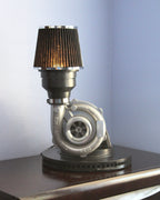 Turbocharger repurposed as a lamp on a wooden surface with a light blue wall background