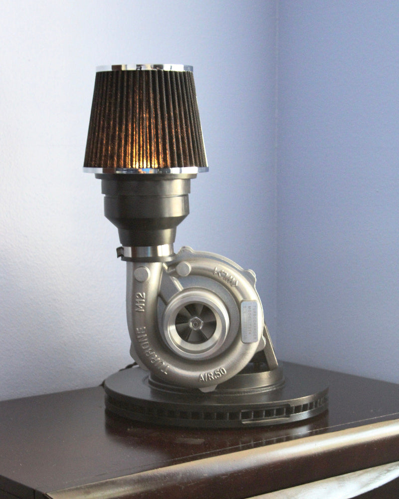 Turbocharger repurposed as a lamp on a wooden surface with a light blue wall background