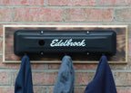 Decorative metal plate with 'Edelbrock' branding on a brick wall with hanging cloths.