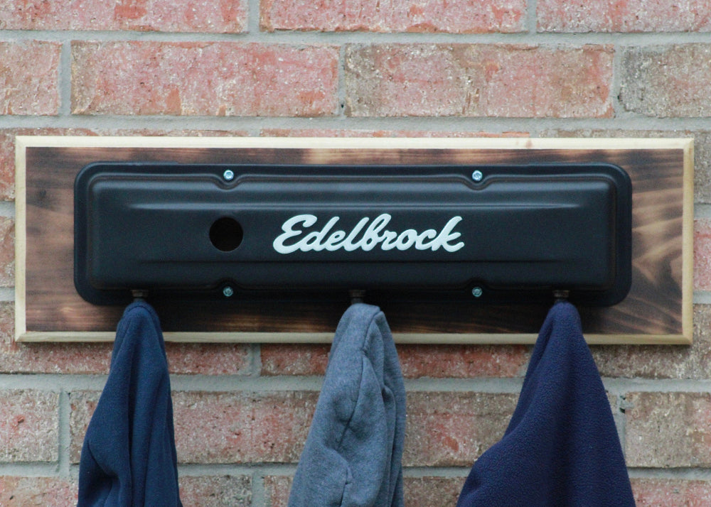 Decorative metal plate with 'Edelbrock' branding on a brick wall with hanging cloths.
