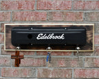 Decorative metal plate with 'Edelbrock' logo on a brick wall.
