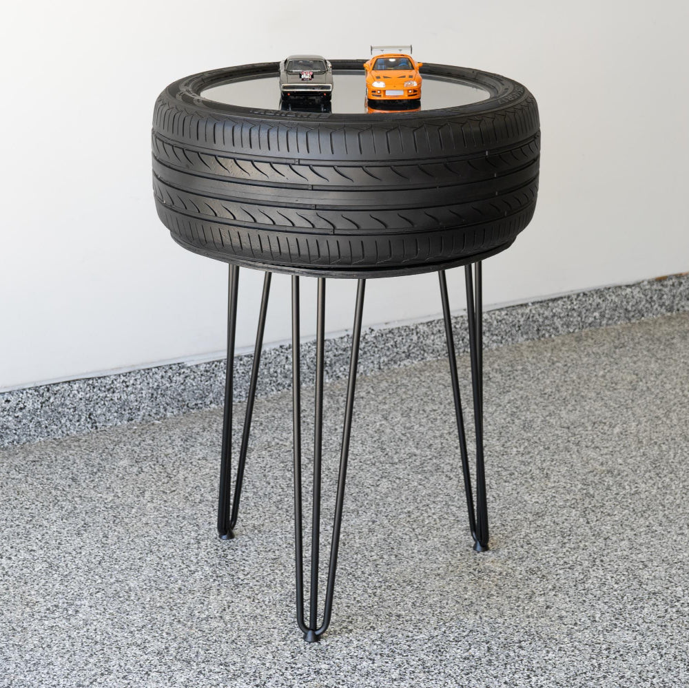 Table made from a recycled tire with hairpin legs on a concrete floor.