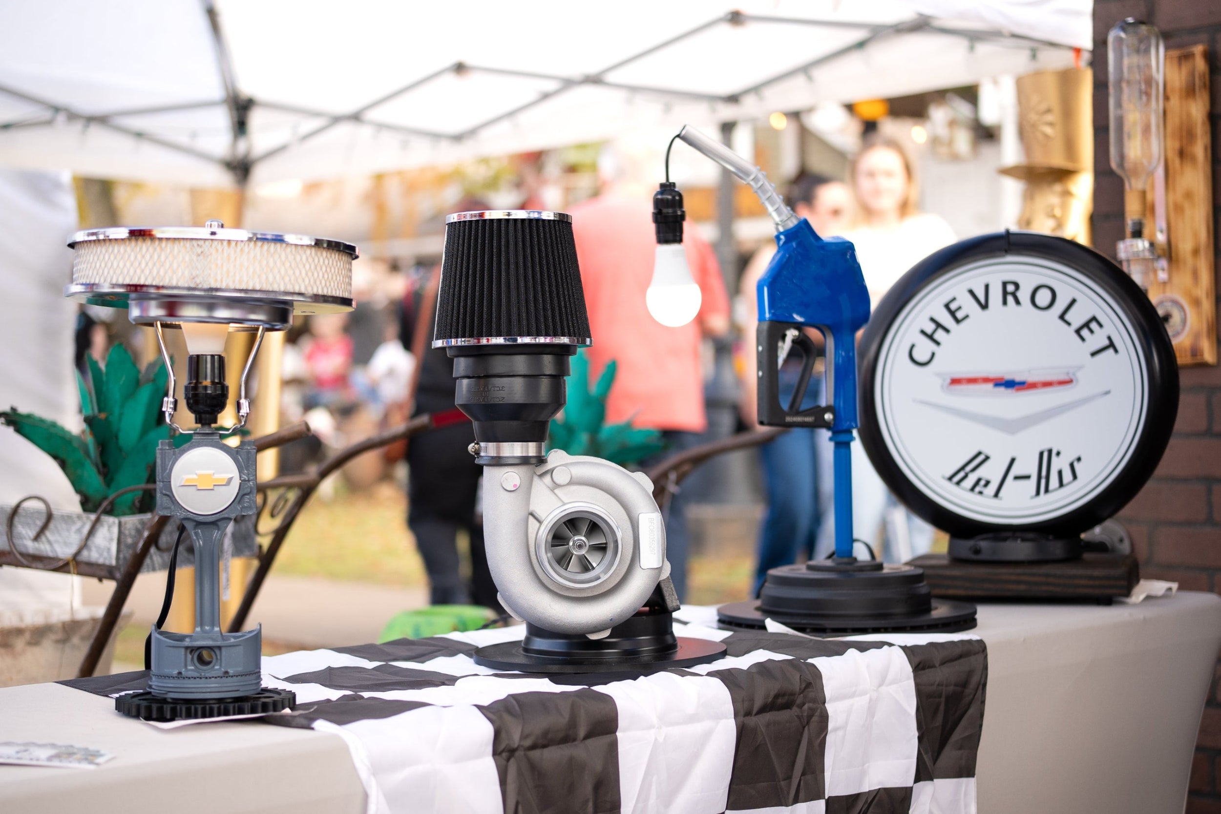 Handcrafted automotive tabletop decor collection including a Chevrolet piston lamp, turbocharger light, gas pump nozzle desk lamp, and illuminated Chevy sign.