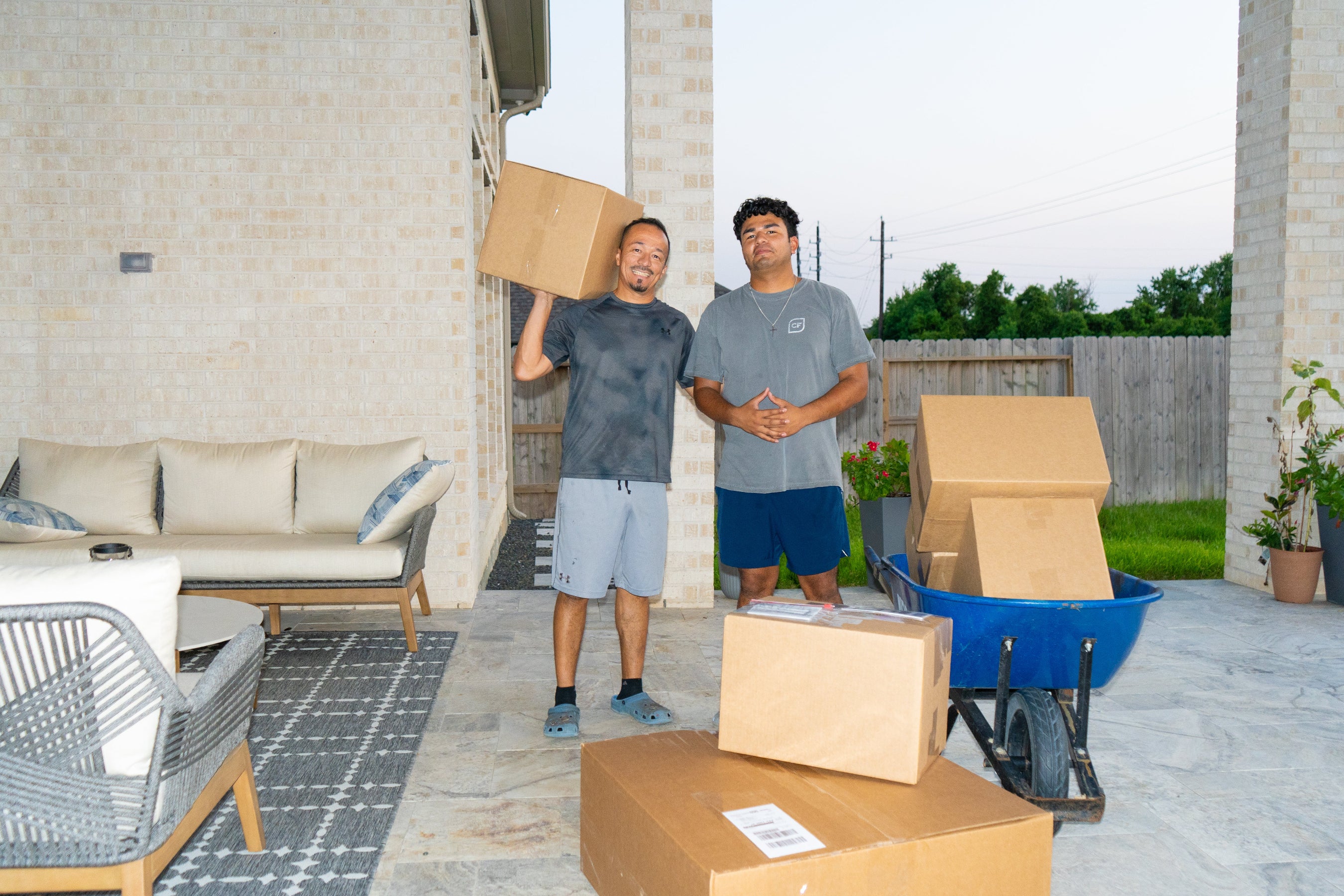 Father and son team standing on a patio surrounded by packaged order boxes and a wheelbarrow ready for shipping.