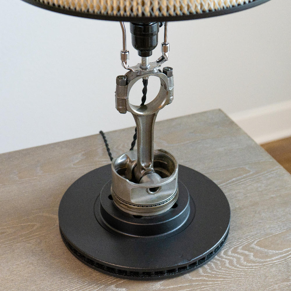 Piston lamp supported by a sandblasted rotor finished in matte black for a clean, industrial foundation.